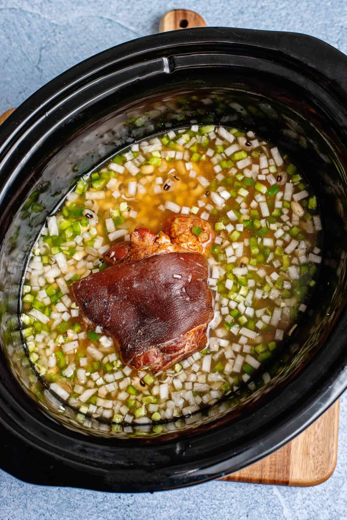Ham hock nestled in the middle of the crockpot with other Hoppin' John ingredients