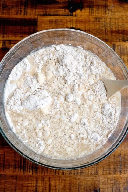 Mixing the wet mixture for the homemade dinner rolls with a wooden spoon