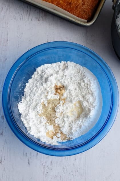 Adding wet ingredients to the bowl of brown butter frosting dry ingredients