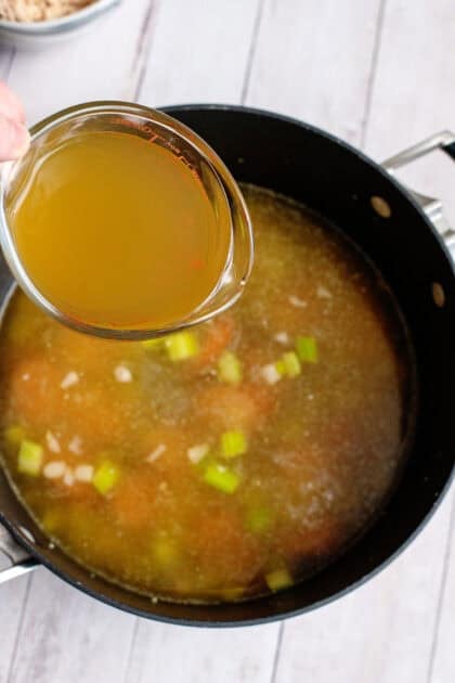 Adding chicken broth to the pot of cooked onion and celery