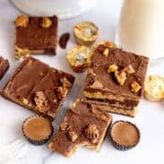 Squares of chocolate peanut butter fudge on a table with peanut butter cup candies