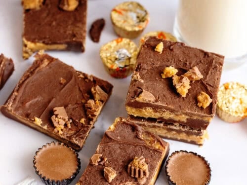 Squares of chocolate peanut butter fudge on a table with peanut butter cup candies