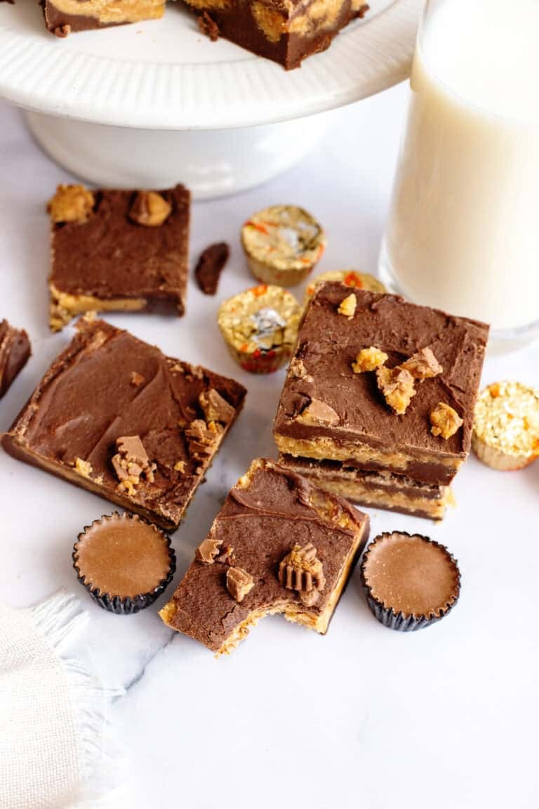 Squares of chocolate peanut butter fudge on a table with peanut butter cup candies