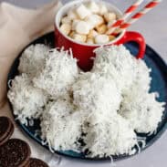 A plate of coconut-coated Oreo balls on a plate with hot cocoa