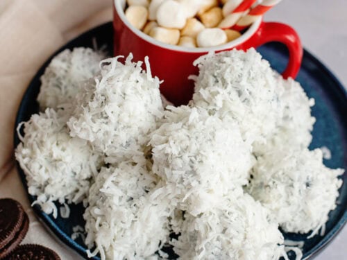 A plate of coconut-coated Oreo balls on a plate with hot cocoa