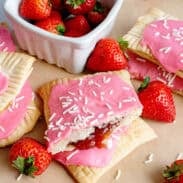 A batch of homemade strawberry pop-tarts near a bowl of fresh strawberries