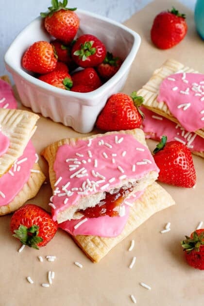 A batch of homemade strawberry pop-tarts near a bowl of fresh strawberries