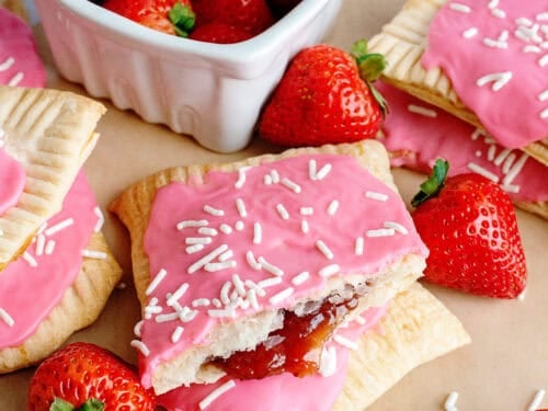 A batch of homemade strawberry pop-tarts near a bowl of fresh strawberries