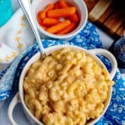 A bowl of veggie mac and cheese next to some baby carrots