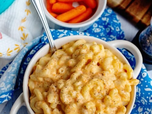 A bowl of veggie mac and cheese next to some baby carrots