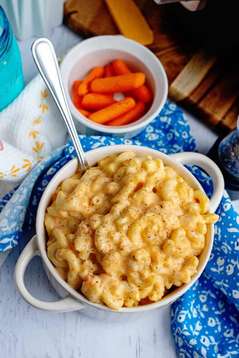 A bowl of veggie mac and cheese next to some baby carrots