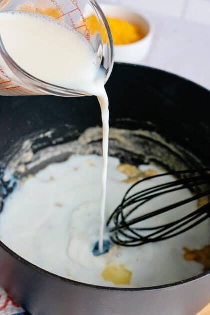 Adding milk to a pan of butter and flour