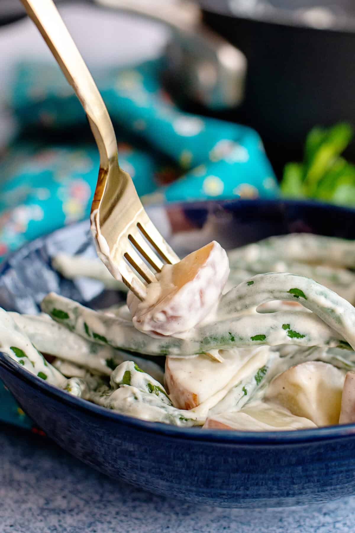 A fork taking a potato from a bowl of creamed beans and taters