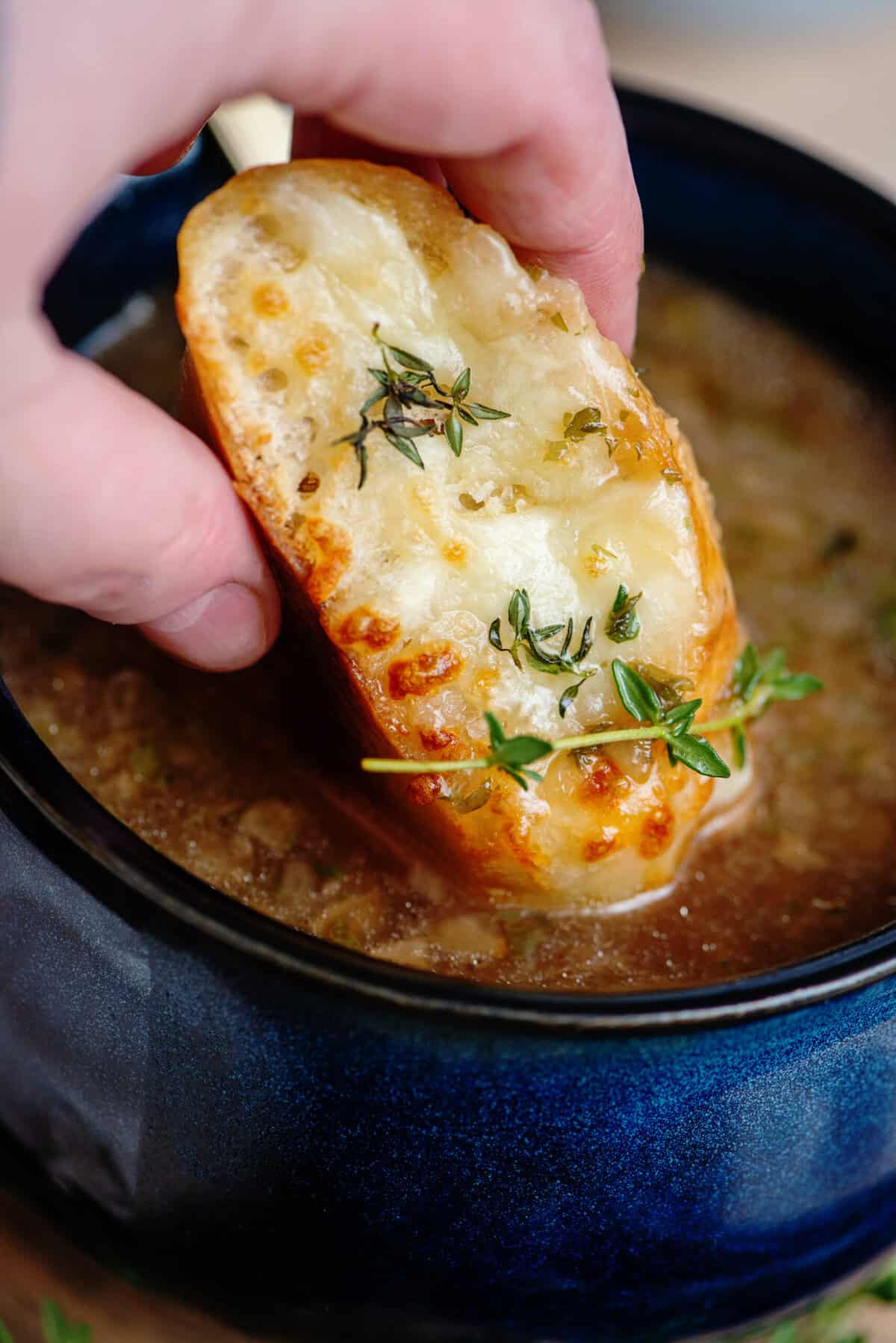 Close up of French bread being dipped into French onion soup