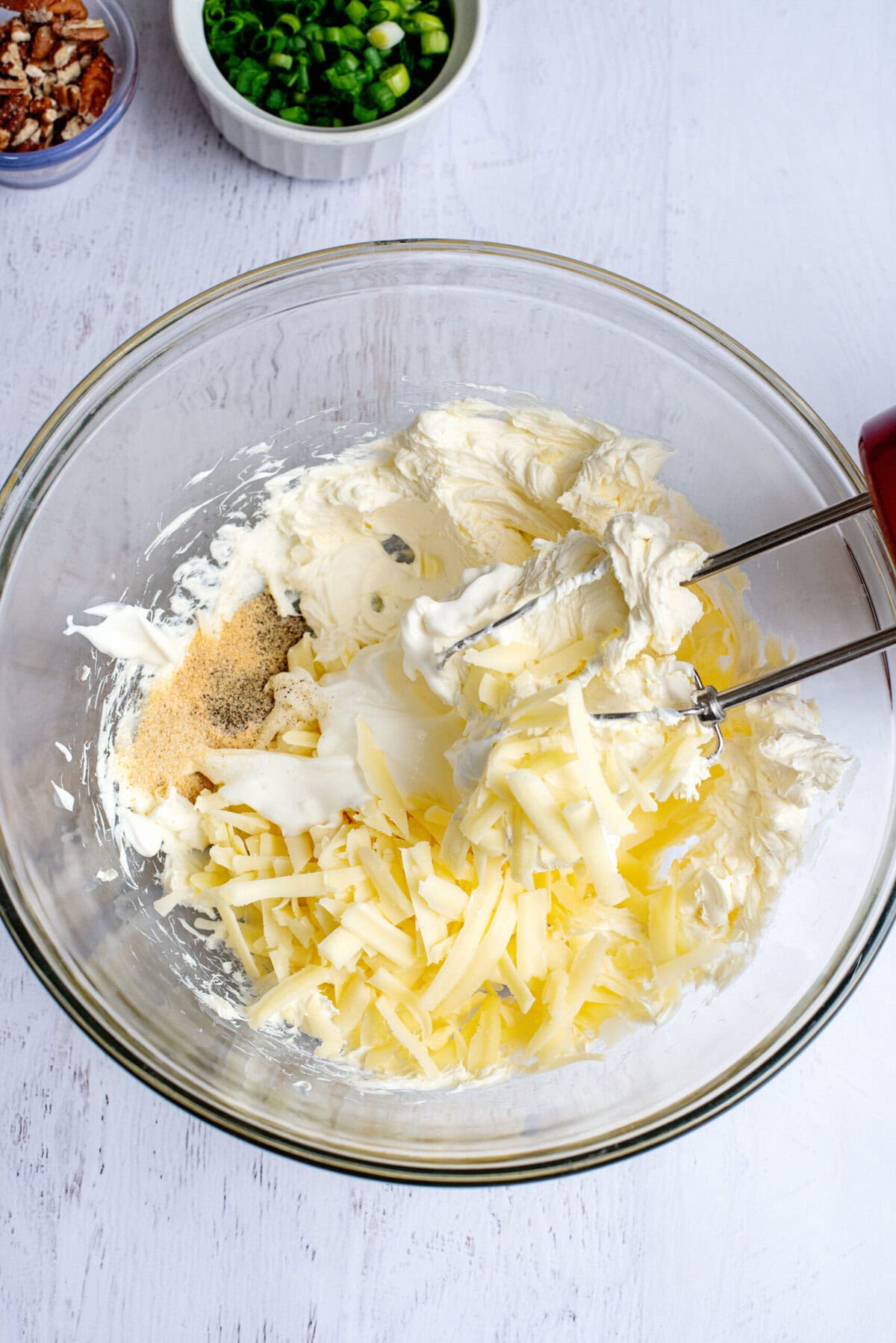 Beating softened cream cheese in a bowl and mixing with shredded cheddar cheese