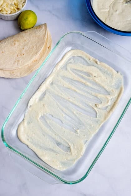 Spreading green enchilada sauce across the baking dish