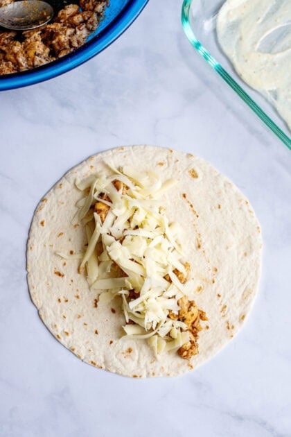 Adding cheese to the chicken mixture on tortillas