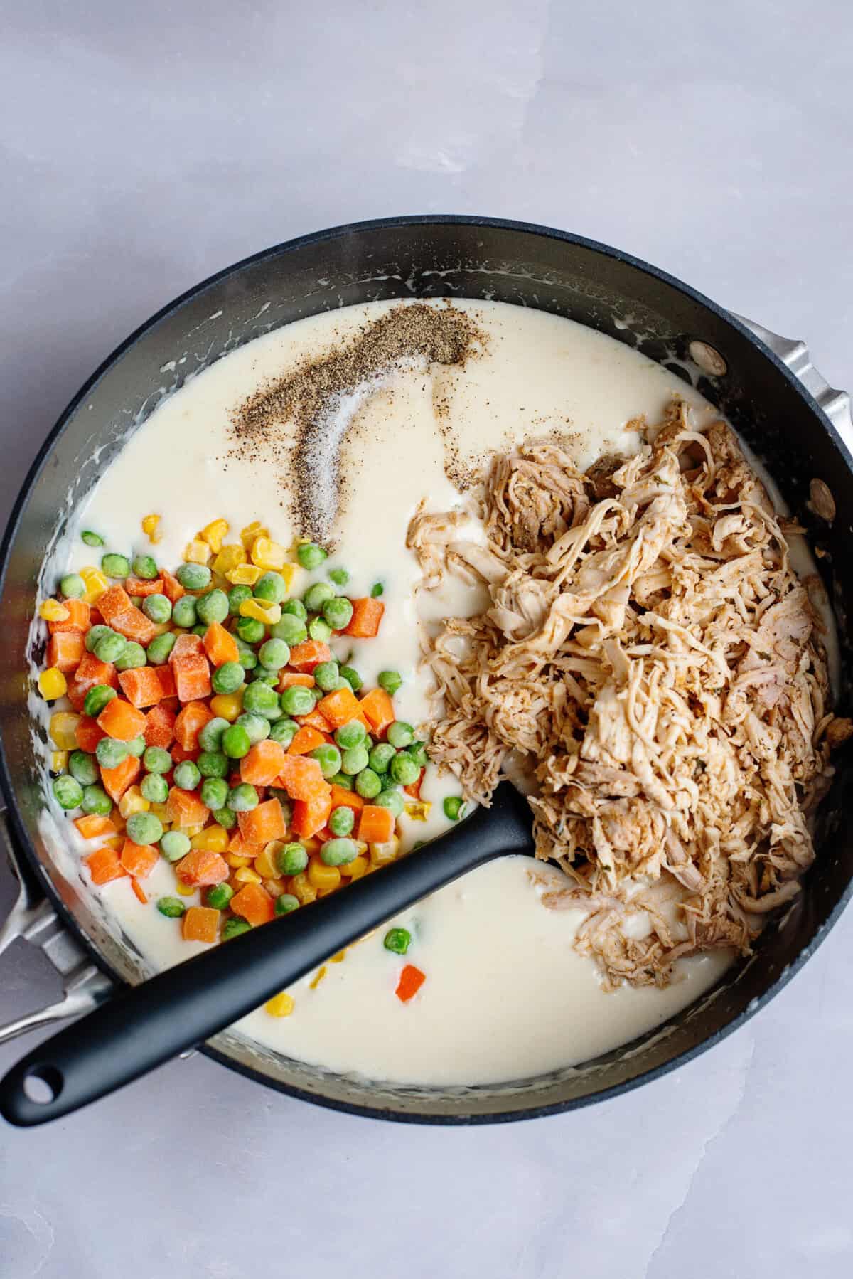 Adding chicken pot pasta filling to the skillet with the creamy sauce