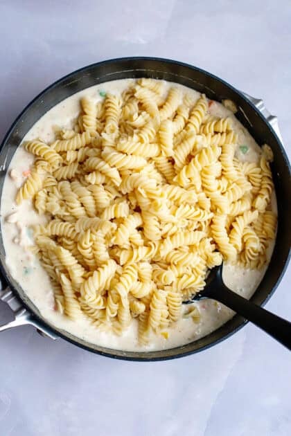 Adding cooked pasta to the skillet of chicken pot pasta filling and creamy sauce