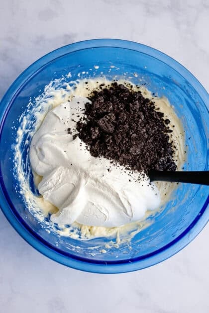 Adding whipped cream and crushed Oreos to a bowl of cream cheese