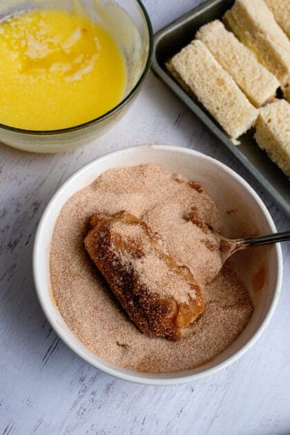 Dipping the stuffed french toast sticks in the bowl of cinnamon and sugar
