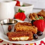 A plate of stuffed French toast sticks with fruits and syrup