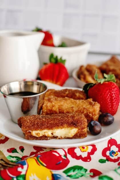A plate of stuffed French toast sticks with fruits and syrup