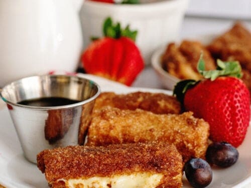 A plate of stuffed French toast sticks with fruits and syrup