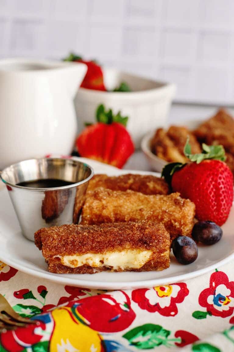 A plate of stuffed French toast sticks with fruits and syrup