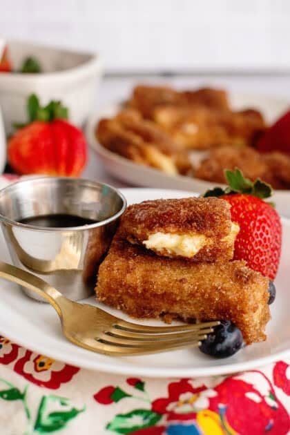 Side view of stuffed French toast sticks on a plate with fruit and syrup