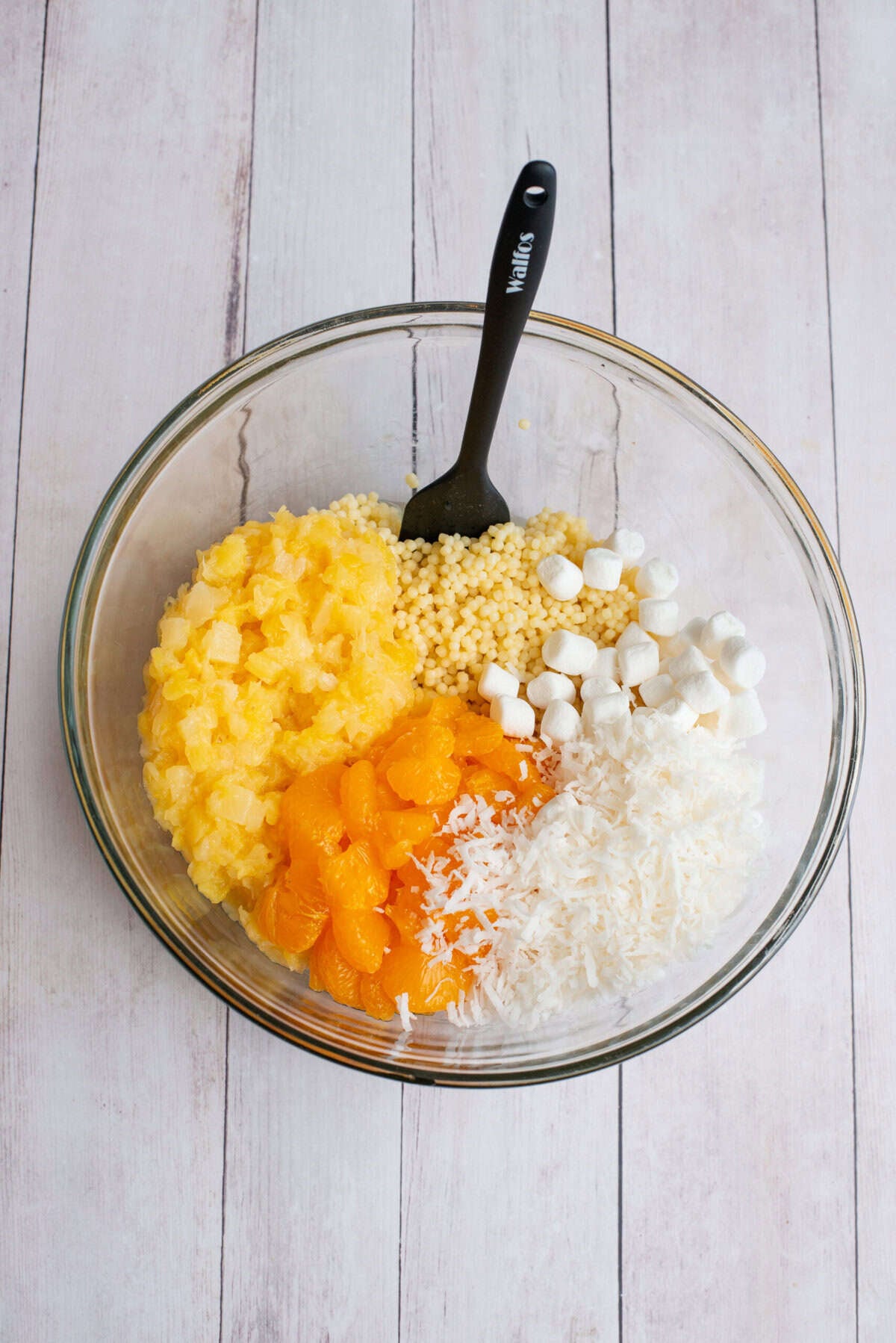 Cooked pasta, the crushed pineapple, mandarin oranges, shredded coconut, and mini marshmallows in a mixing bowl