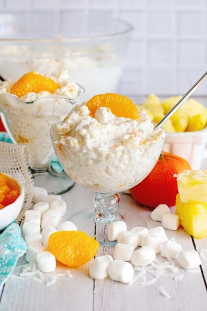 2 glasses of Frog Eye Salad with marshmallows and other ingredients in the background