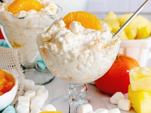 2 glasses of Frog Eye Salad with marshmallows and other ingredients in the background