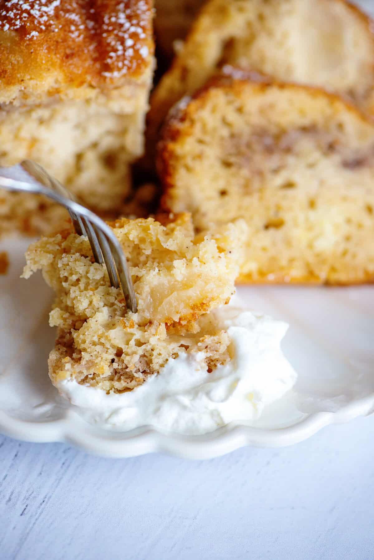 A bite of pear bundt cake being dipped into whipped cream