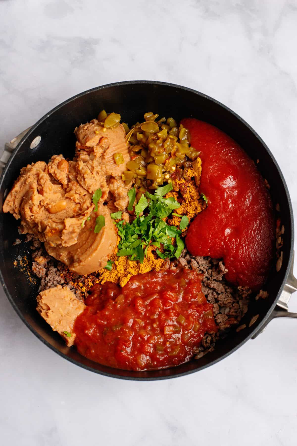 Refried beans, green chilies, taco seasoning, cilantro, salsa, and tomato sauce in a pan