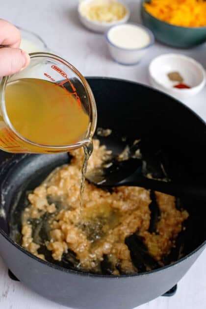 Pouring chicken broth into a pan of onion and garlic