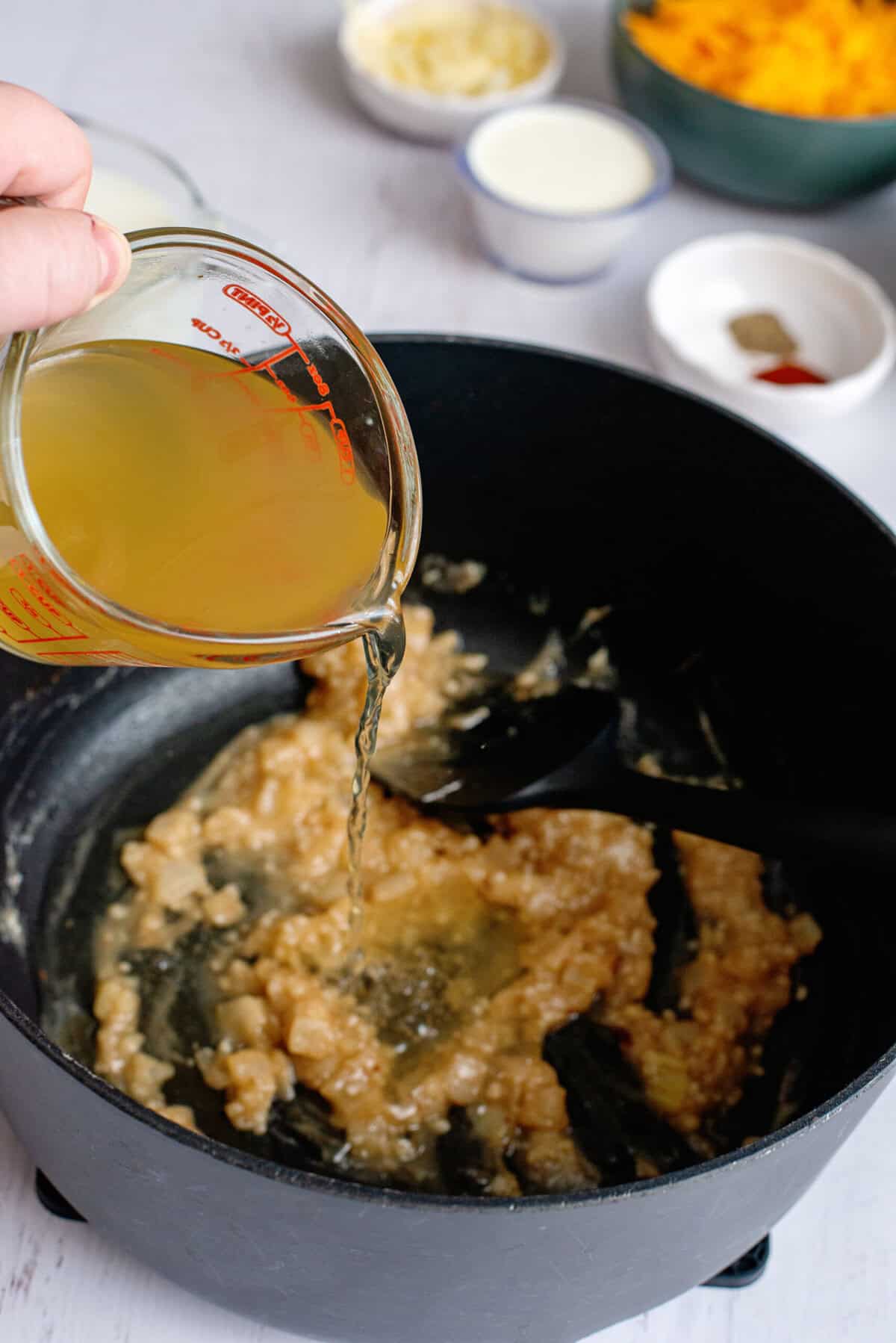 Pouring chicken broth into a pan of onion and garlic