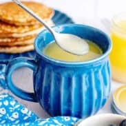 Homemade maple syrup in a blue mug with a spoon scooping out some from it.