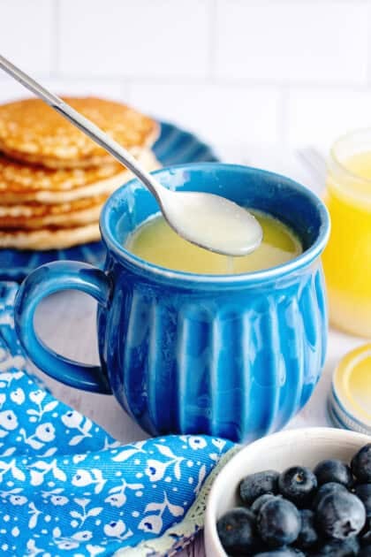 Homemade maple syrup in a blue mug with a spoon scooping out some from it.