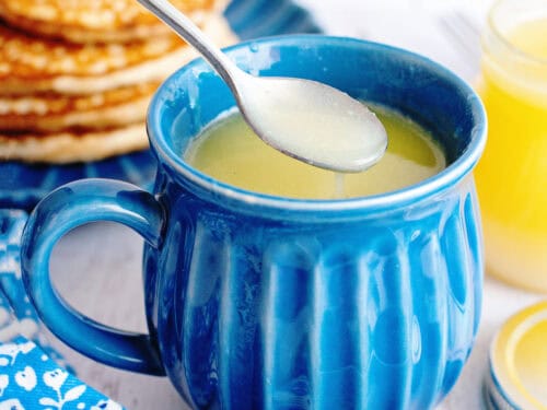 Homemade maple syrup in a blue mug with a spoon scooping out some from it.