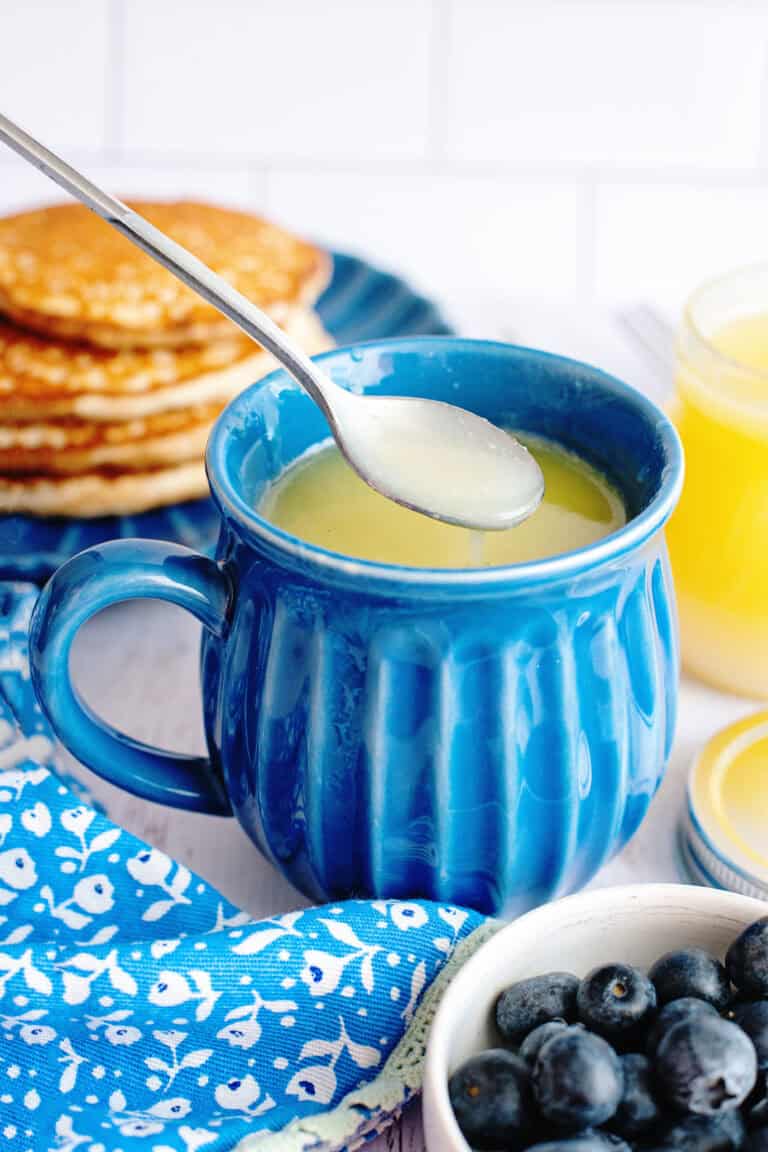 Homemade maple syrup in a blue mug with a spoon scooping out some from it.