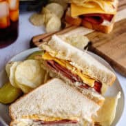 A plate with sliced fried bologna sandwich and chips