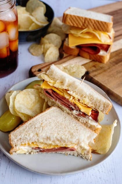A plate with sliced fried bologna sandwich and chips