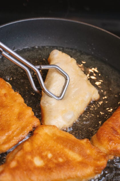Using tongs to turn the beignets in the frying pan