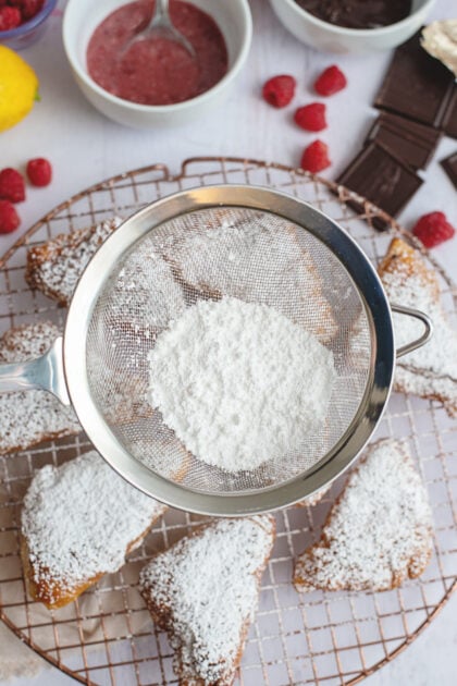 Dusting the beignets with powdered sugar while they cool on a wire rack