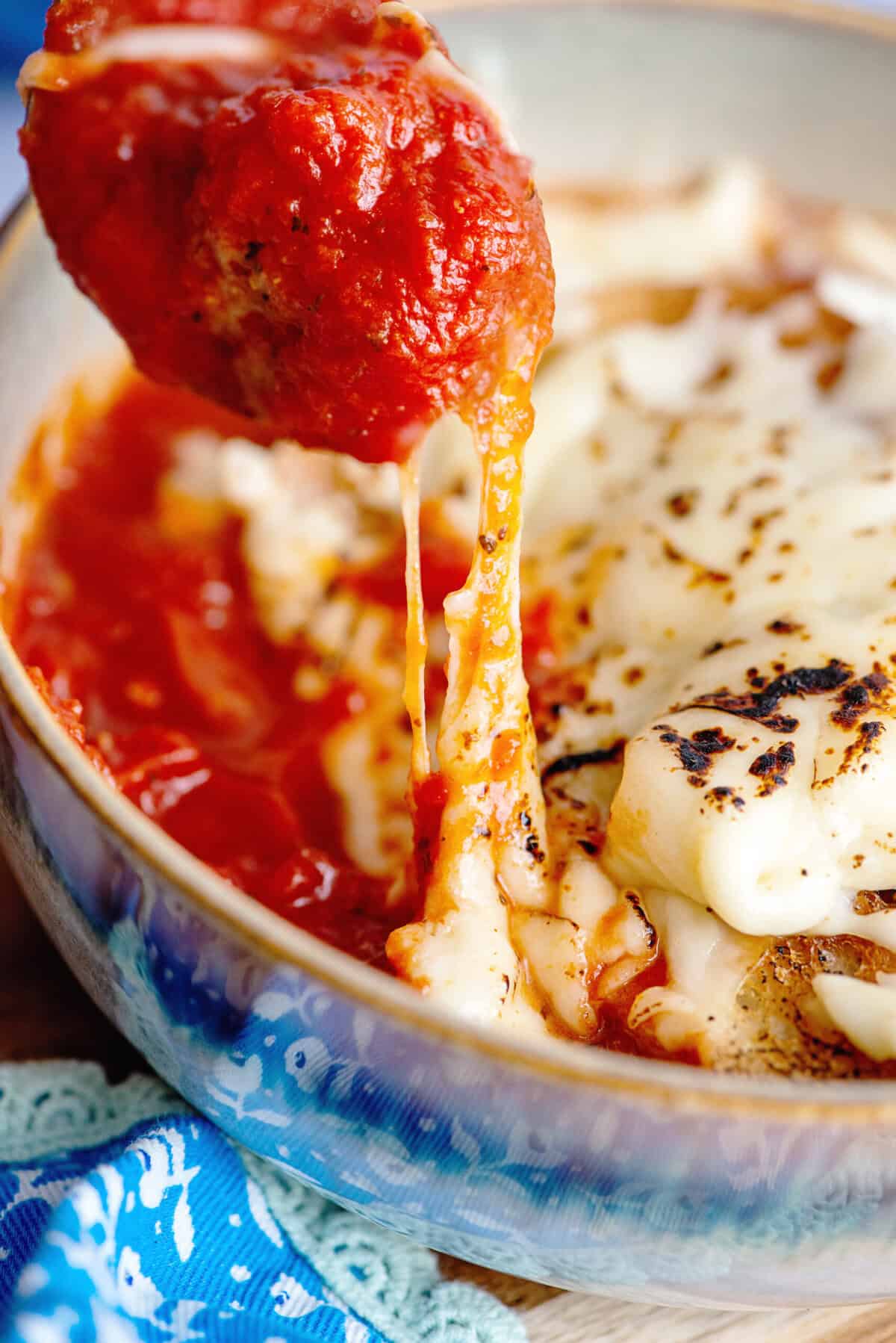 Taking a meatball from a bowl of pizza soup with a spoon