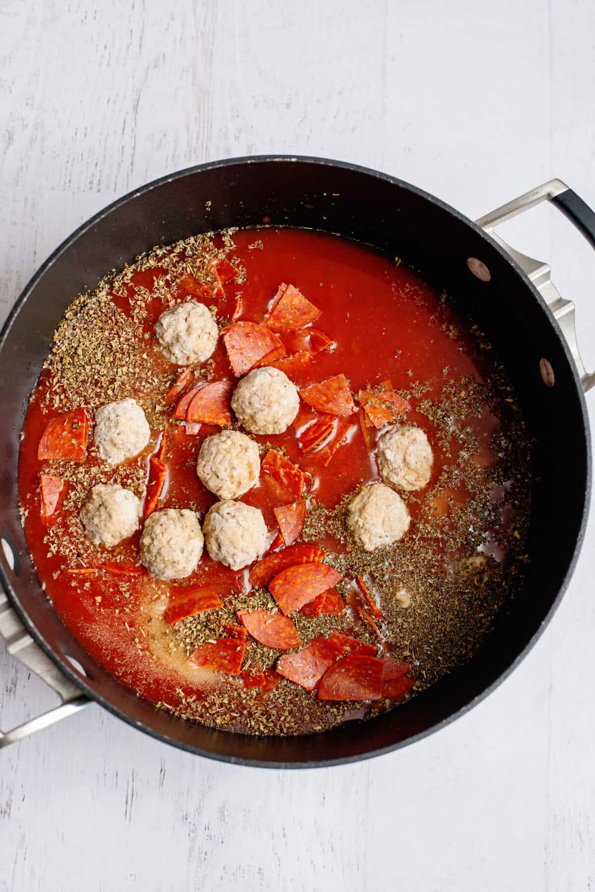 Adding meatballs to the pot with sauce and seasoning