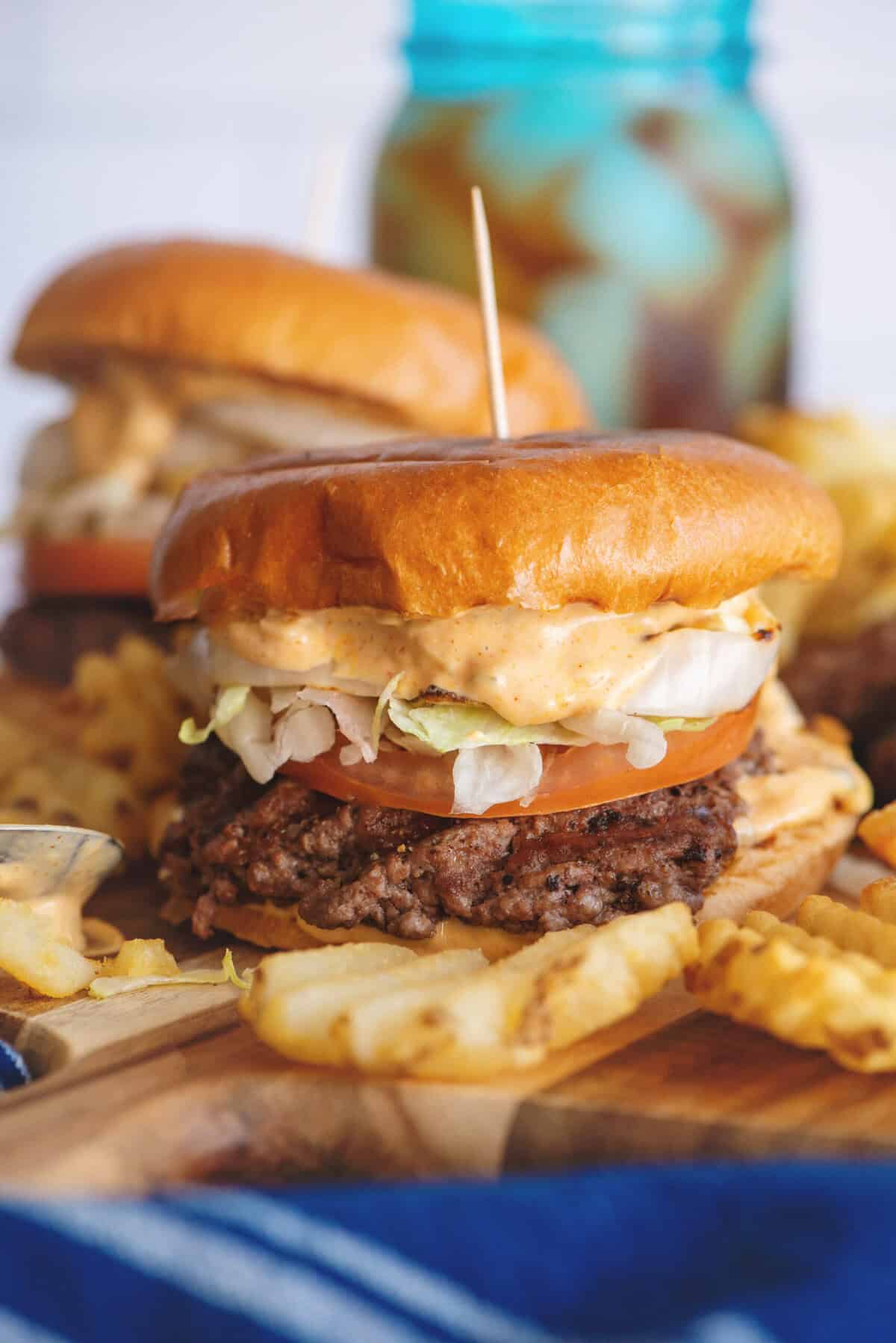 Smash burgers on a serving board with waffle fries.