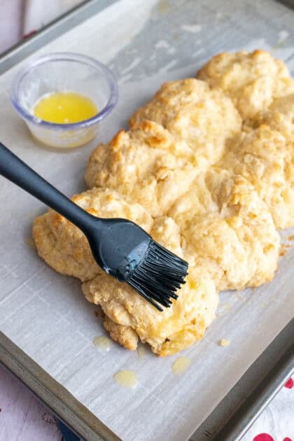 Baked cathead biscuits being brushed with butter