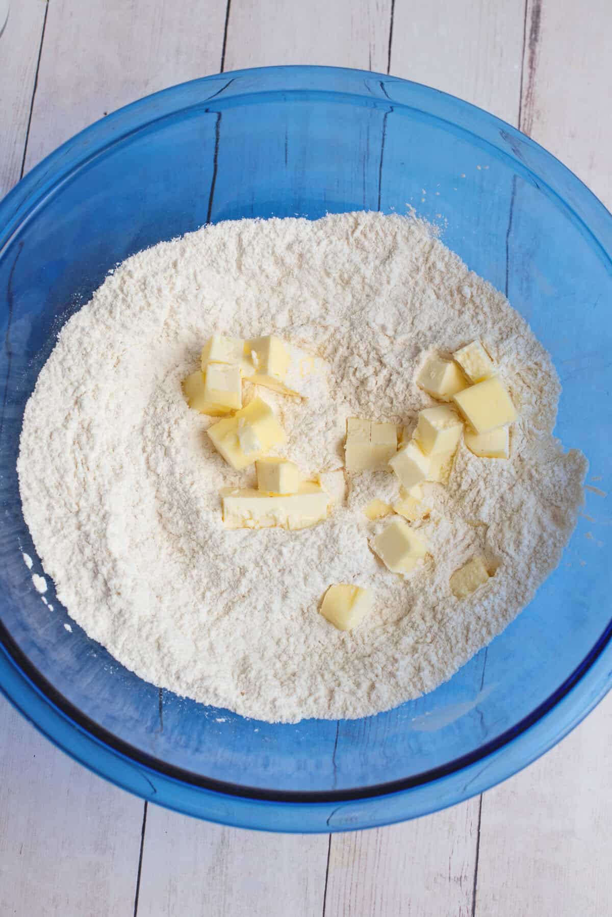 Adding butter to the small mixing bowl of dry ingredients for cathead biscuits